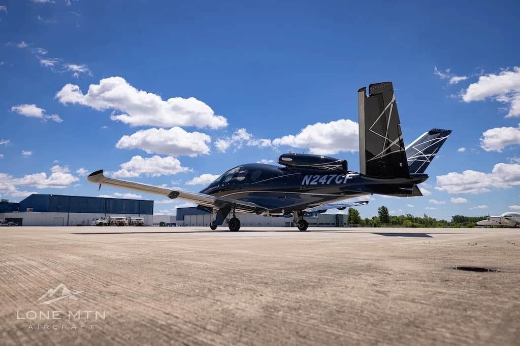 A black Cirrus Vision Jet (N247CF) with a distinctive tail design parked on a tarmac with buildings in the background.