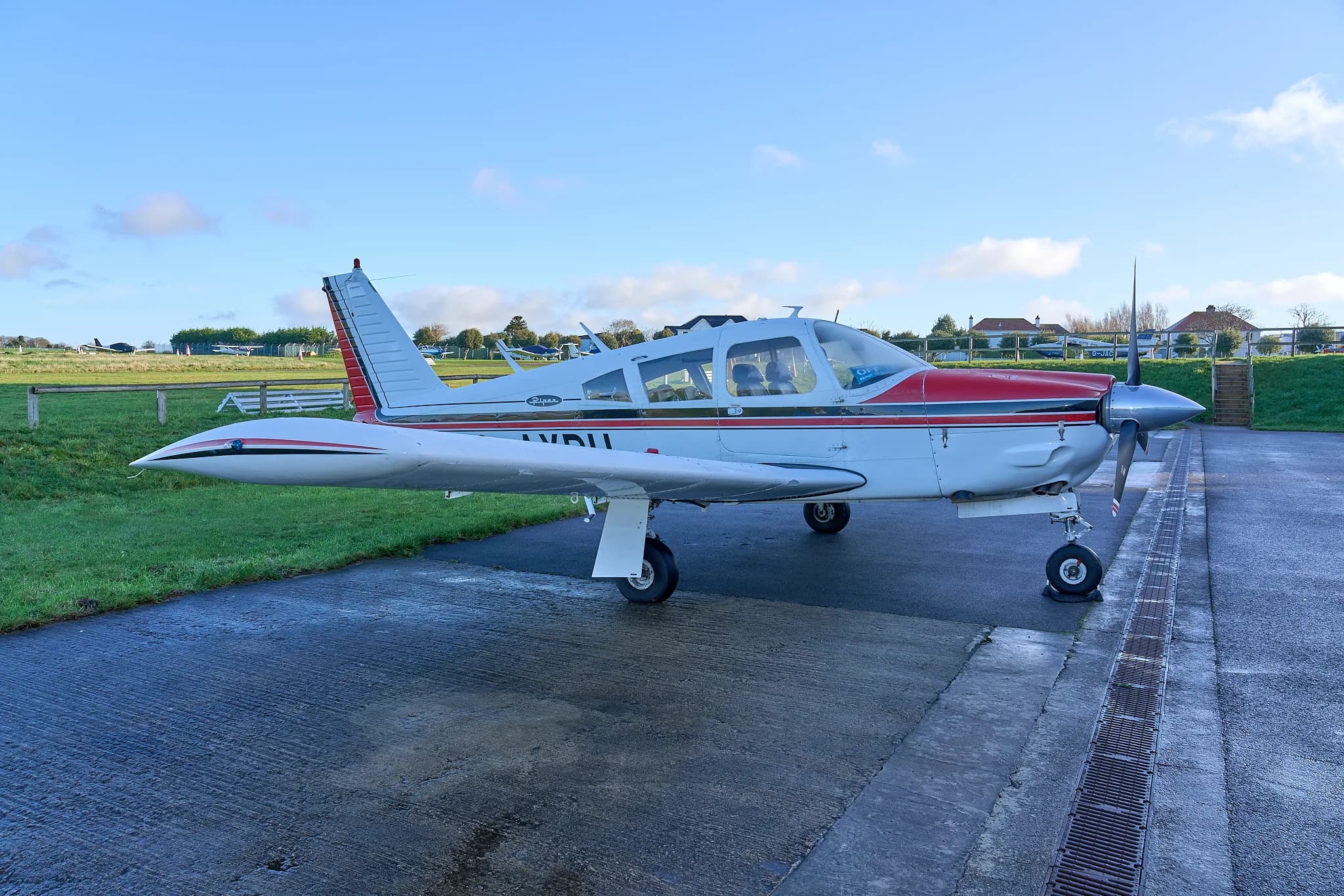 A side view of the white and red Piper Cherokee G-AYPU parked on a wet tarmac.