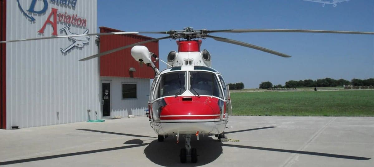 Front view of a red and white helicopter on a tarmac in front of a hangar.
