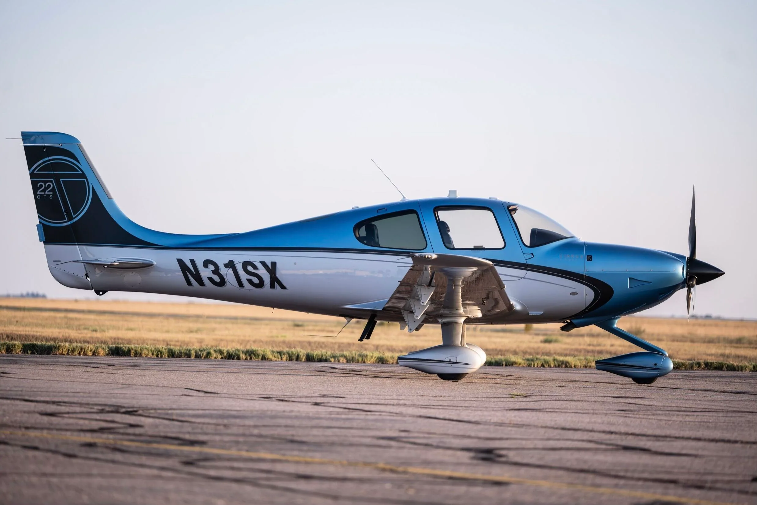 A close-up side view of a Cirrus SR22T aircraft, N31SX, in blue and silver paint, parked on an airfield.