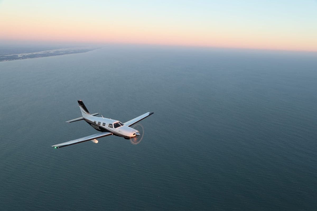 Piper M350 flying over the ocean at sunset.