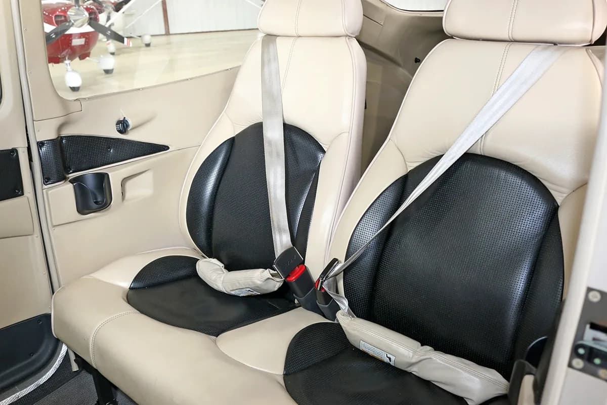 Two beige and black leather aircraft seats with seatbelts are shown in the cabin.