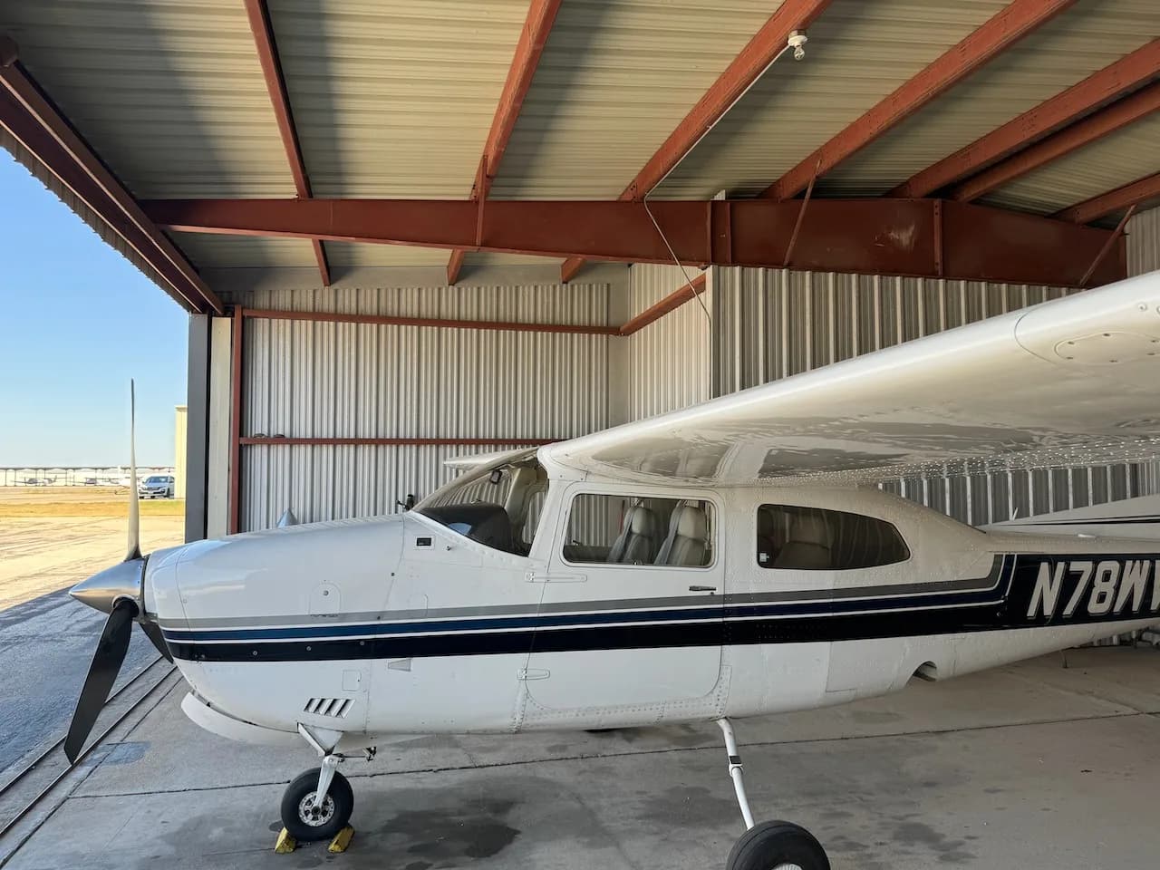 A white Cessna aircraft with blue and black stripes, registration N78WV, parked in a hangar.