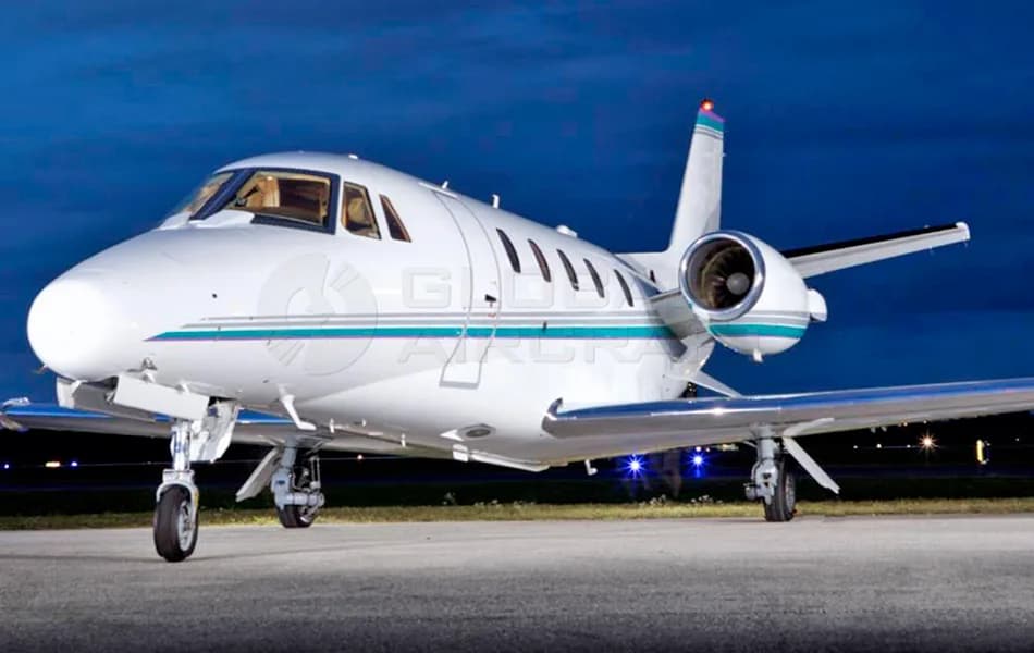 A white business jet with teal and grey stripes parked on a tarmac at night.
