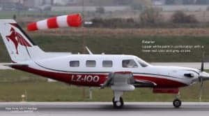 A Piper PA-46-500TP Meridian aircraft with a white and red paint scheme on the tarmac with a windsock in the background.