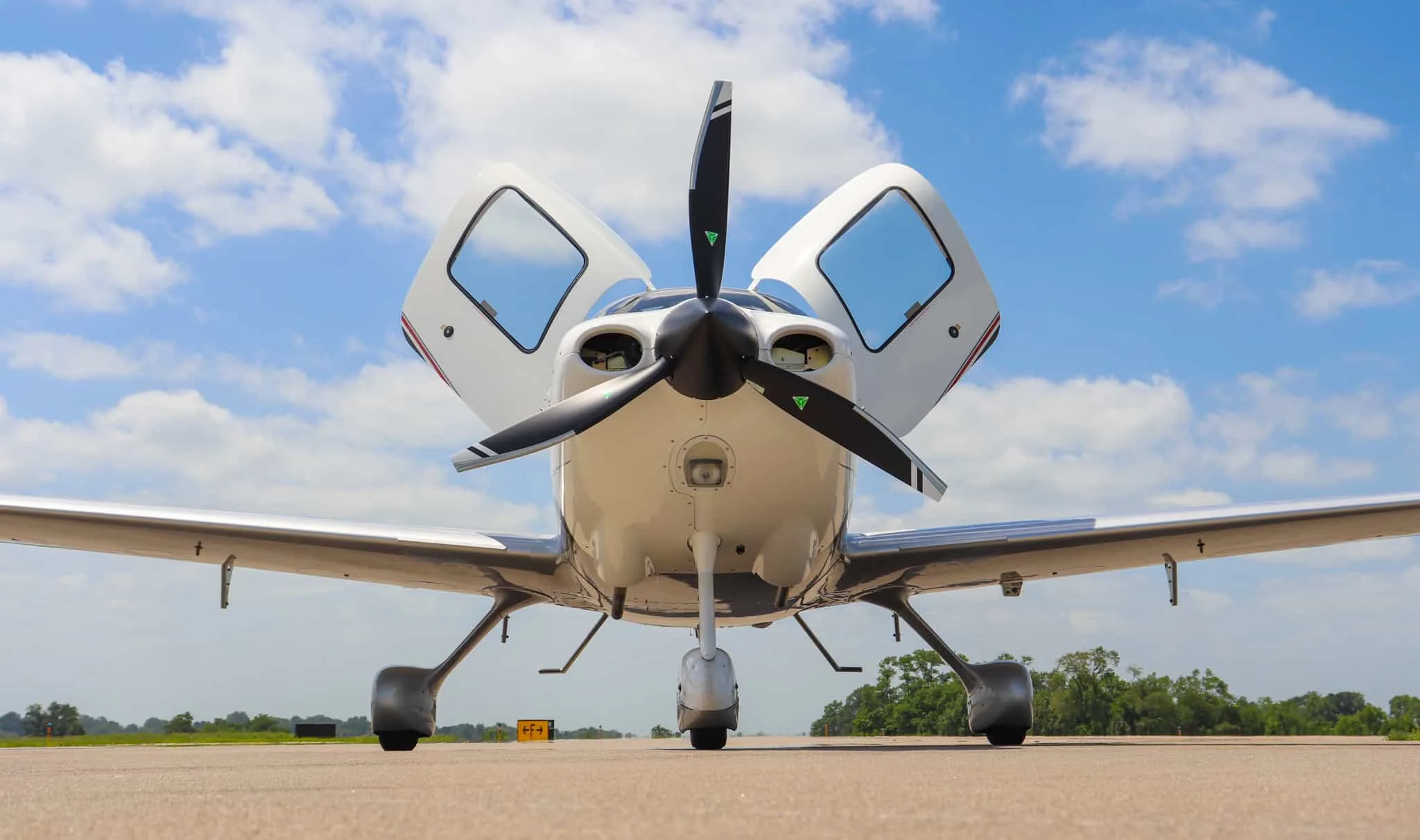 A head-on view of a white Cirrus SR20 X Edition with open doors and a three-bladed propeller.