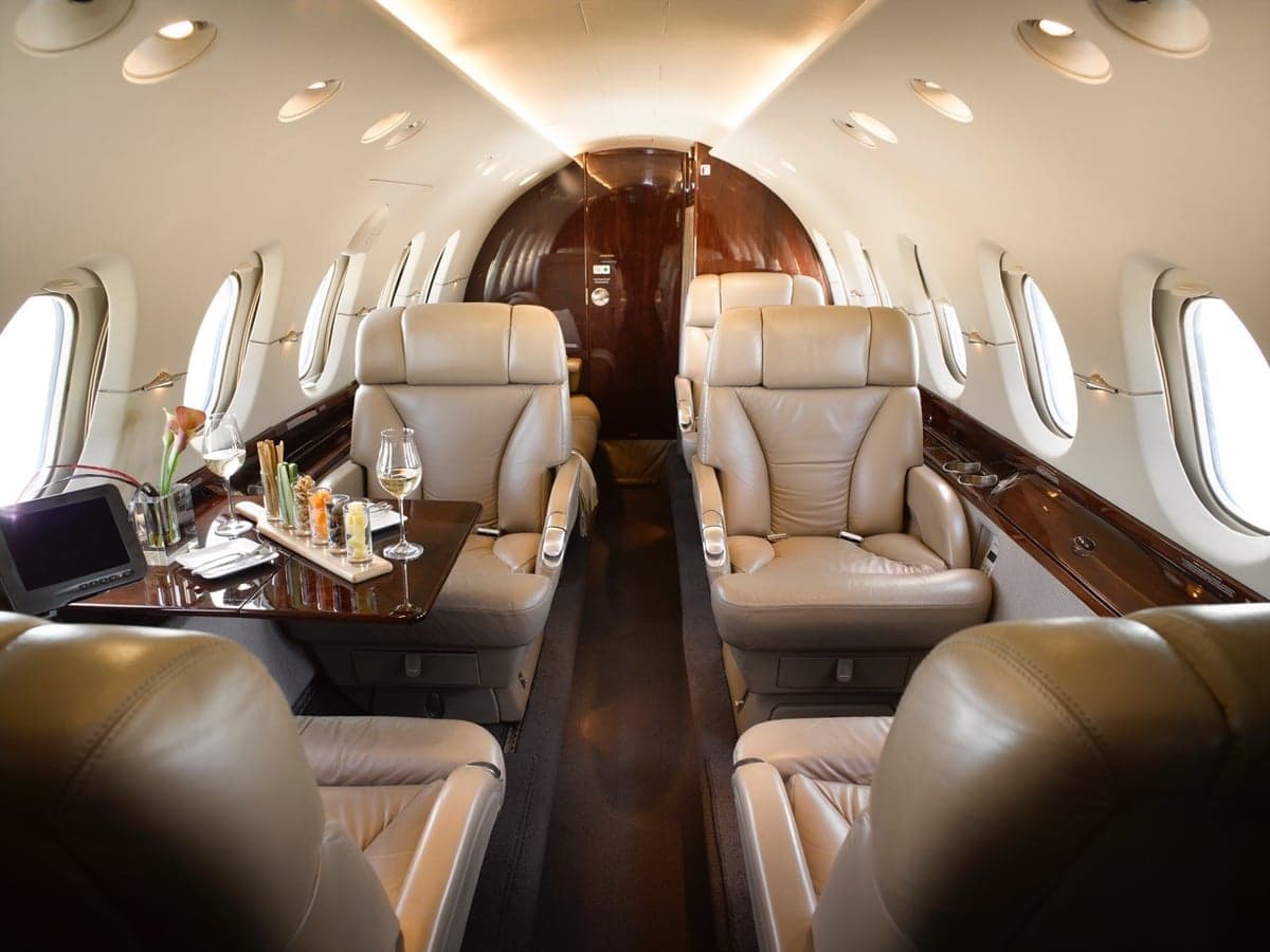 The luxurious interior of a private jet features tan leather seats and a table with drinks.