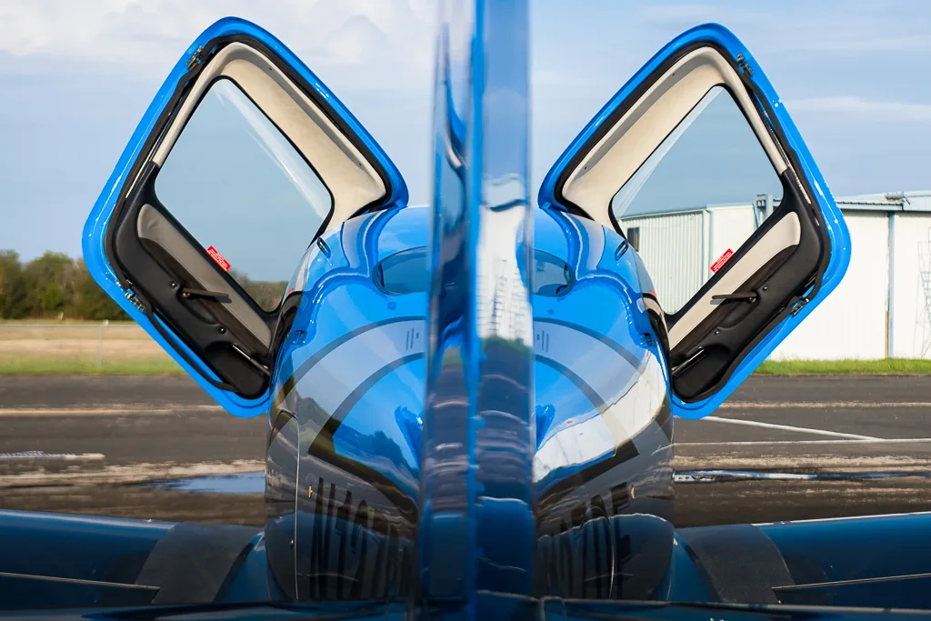 A rear view of the blue and silver Cirrus SR22T GTS Carbon aircraft (N127DF) with both doors open, reflecting the sky.