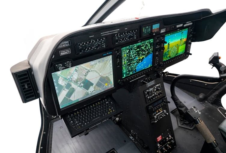 The cockpit of a Bell 505 helicopter, featuring multiple display screens and a keyboard.
