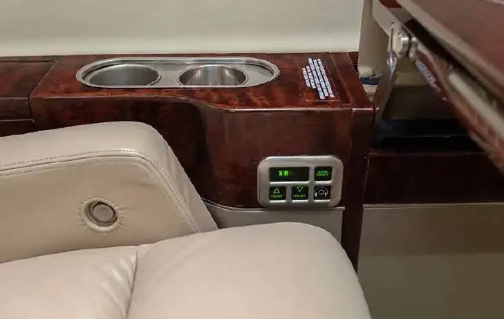 A close-up of a passenger control panel with green illuminated buttons and dual cup holders in the aircraft cabin.