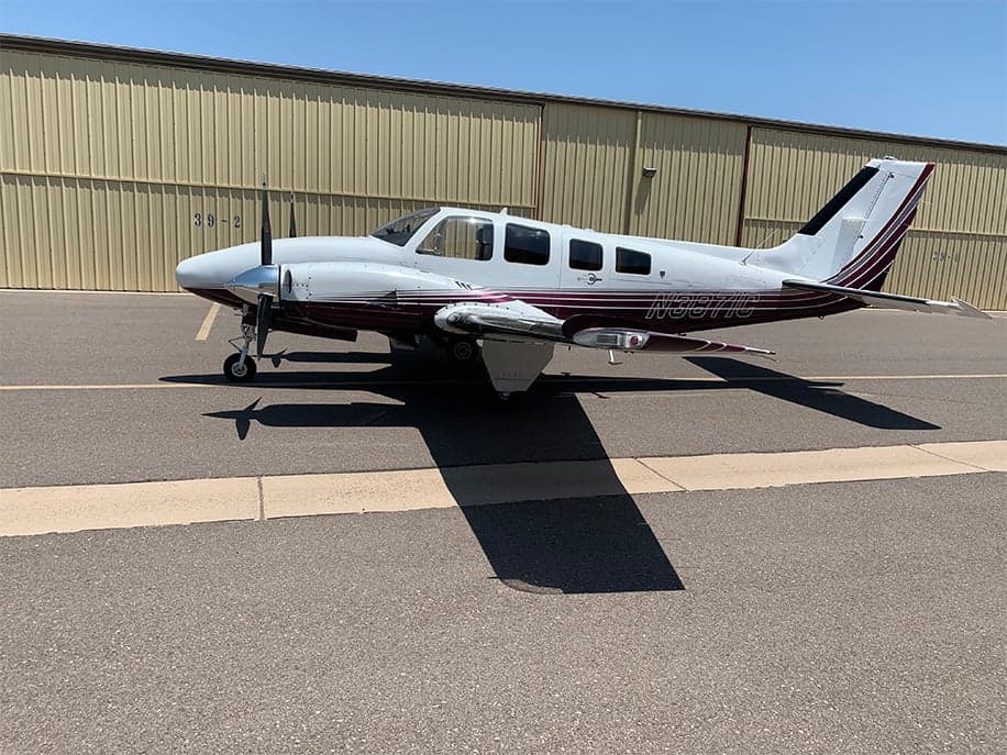 Side view of the N3871C aircraft on the tarmac with a white and burgundy paint scheme.