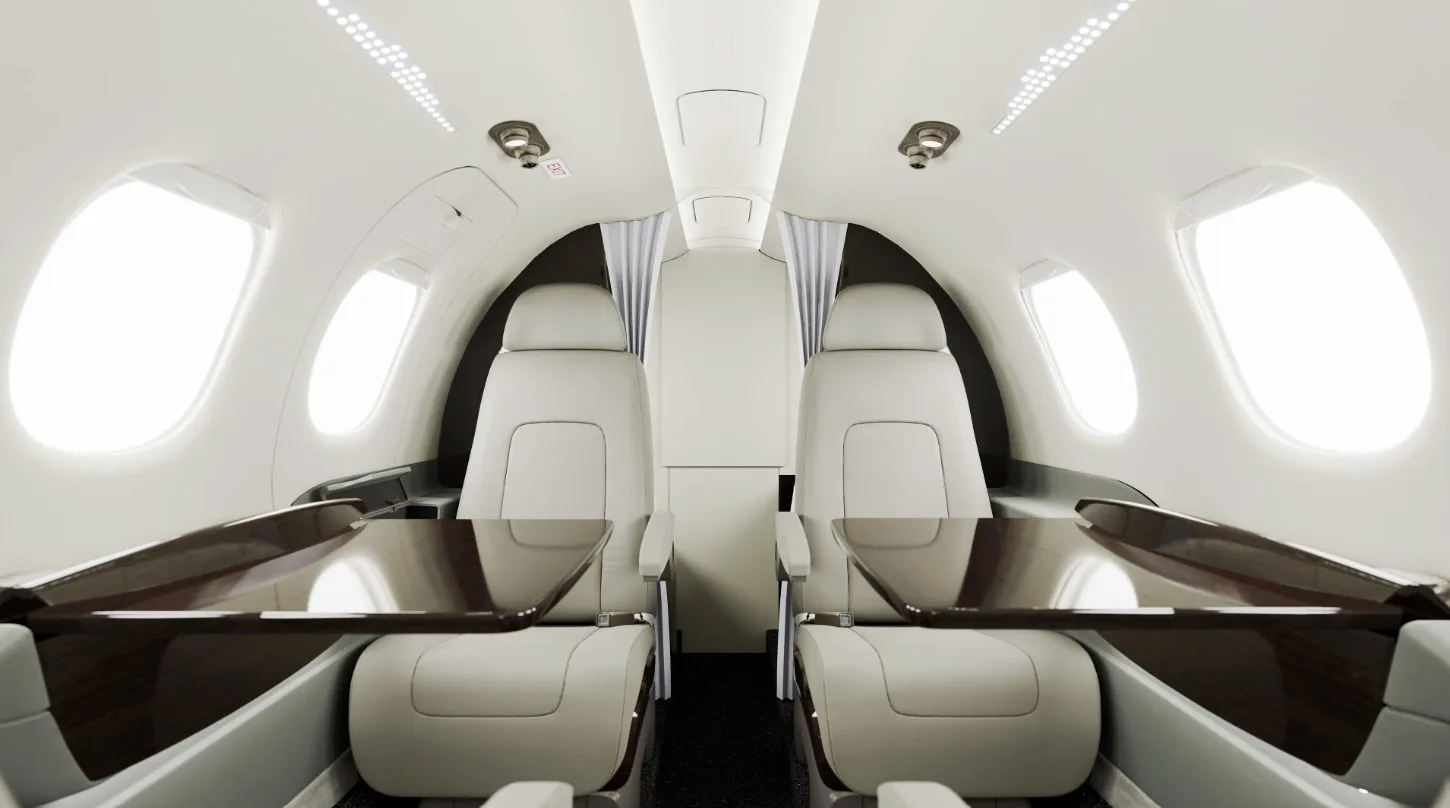 The luxurious interior cabin of a business jet, featuring light leather seats and dark wood tables.