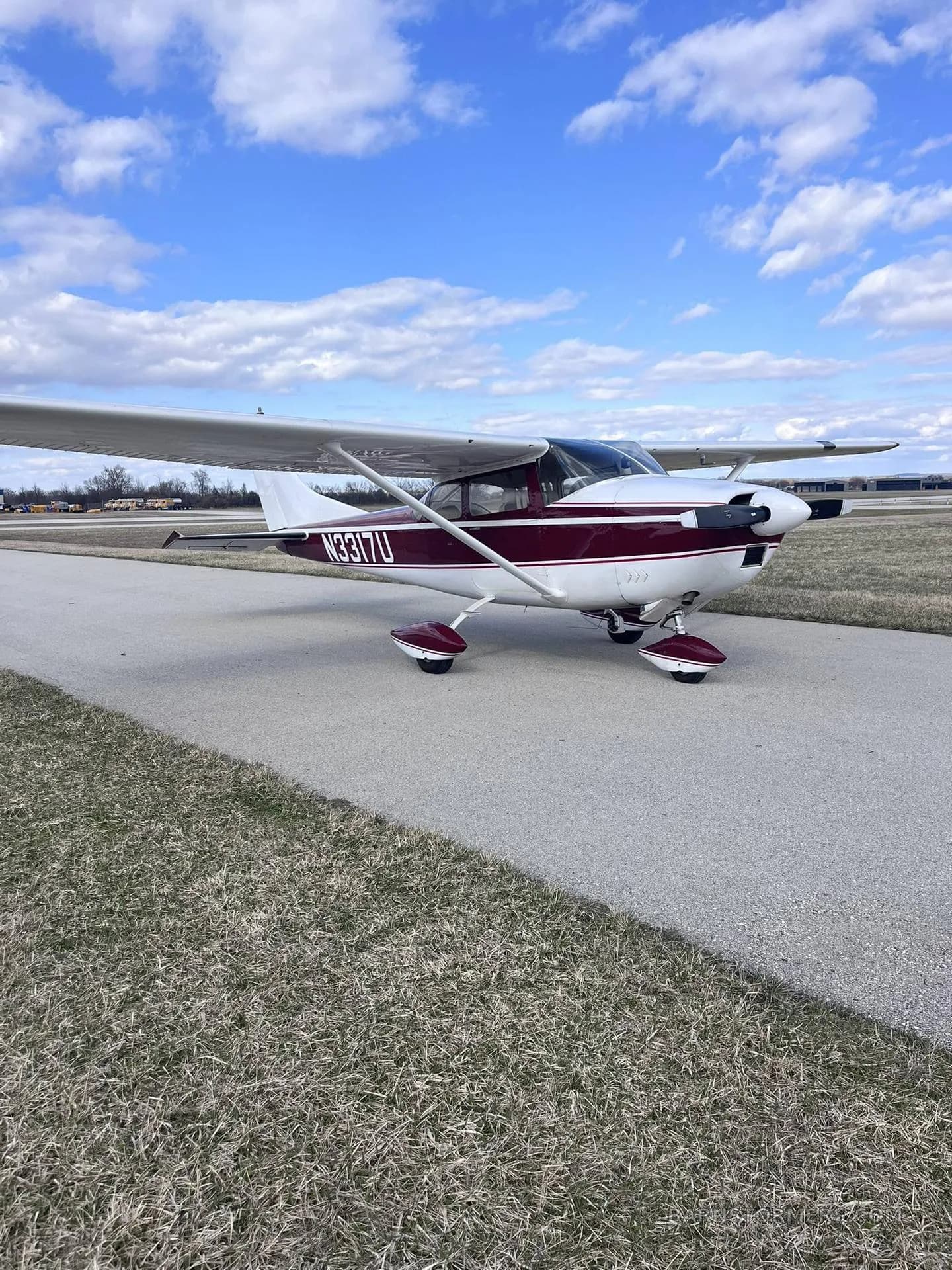 A maroon and white single-engine propeller aircraft (N3317U) parked on an asphalt taxiway with a clear blue sky.
