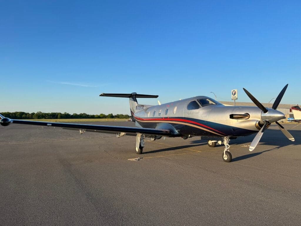 A Pilatus PC-12 with a silver and red paint scheme parked on the tarmac.