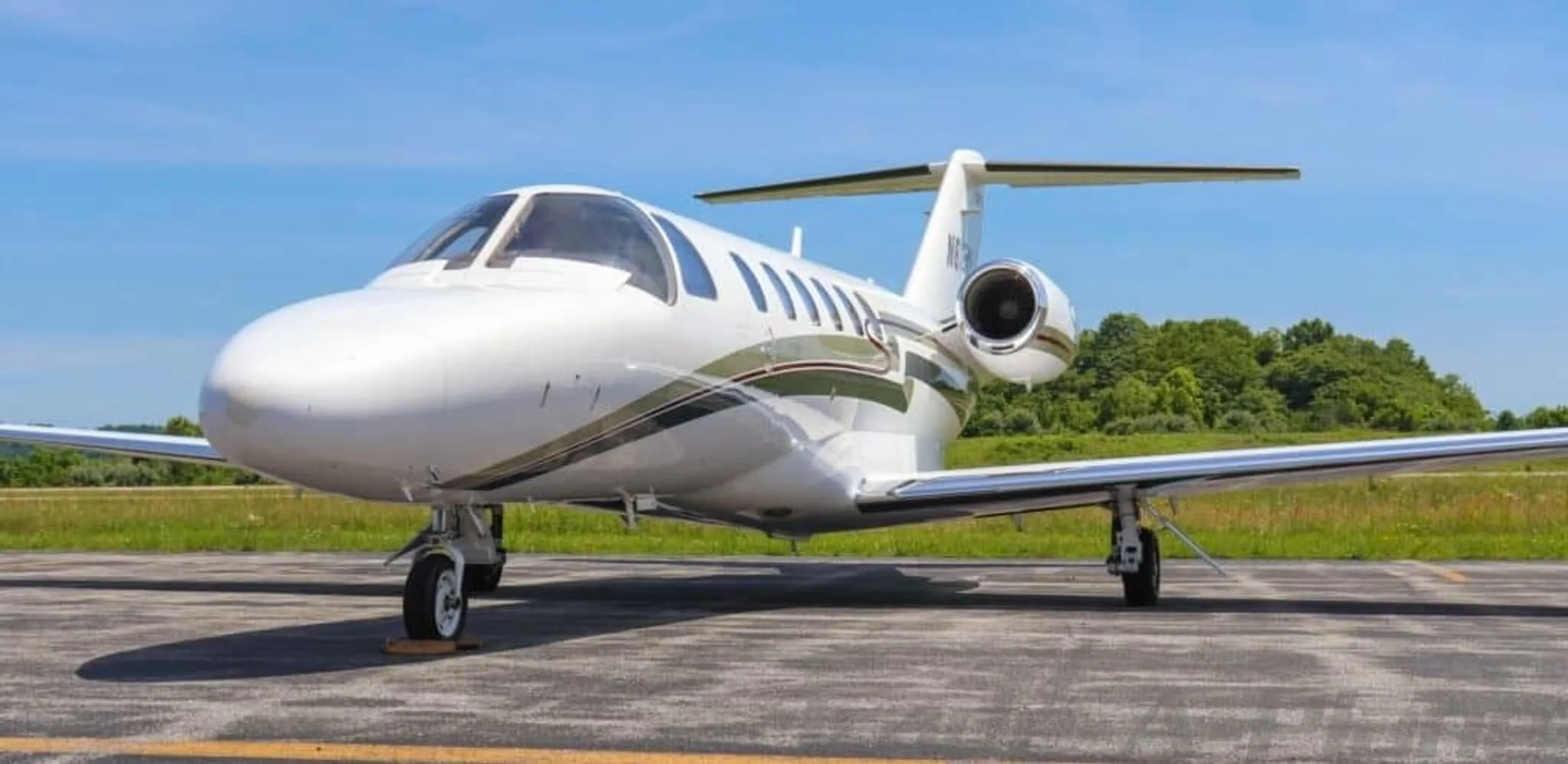 A front-quarter view of a white Cessna Citation CJ2+ business jet with green and red stripes on an airfield.