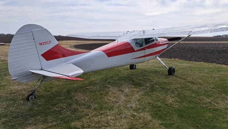 Rear quarter view of a red and white Cessna on a grassy field.
