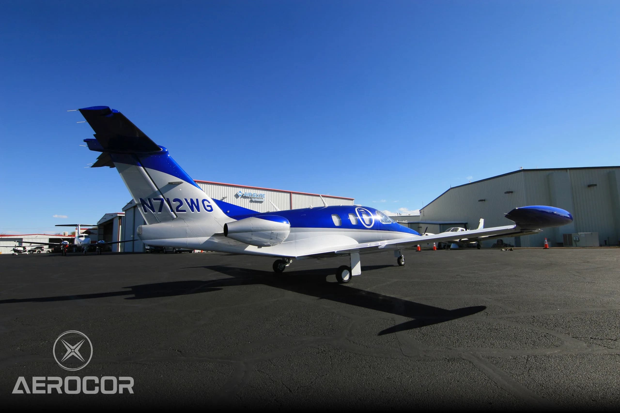 A side view of the blue and white Eclipse 500/550 jet, N712WG, parked in front of a hangar.