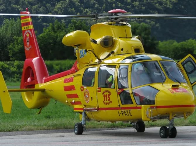 A yellow and red Airbus Helicopters Dauphin AS365 N2 emergency services helicopter with '115 TRENTO' markings on an airfield with trees in the background.