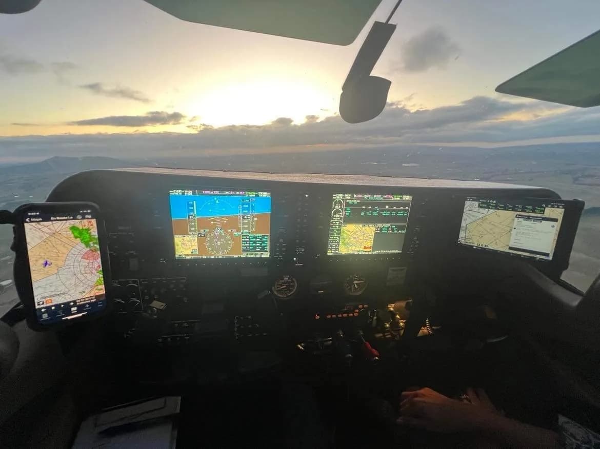 A modern glass cockpit with multiple screens and a phone mount, showing a sunset view from the aircraft.