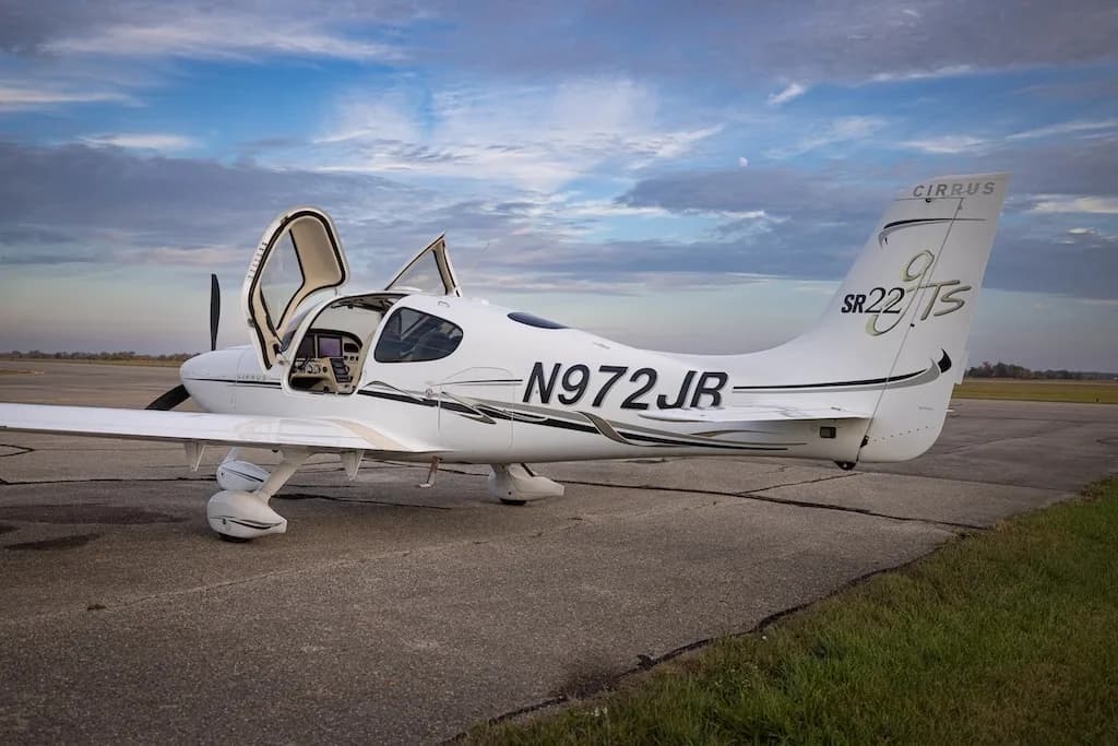 The rear-left side of a white Cirrus SR22T aircraft, N972JB, is shown parked on an airfield with its doors open.