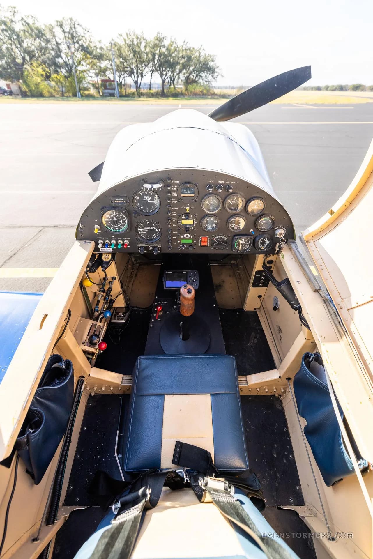 The cockpit of a single-seat aircraft showing the instrument panel, stick, and blue and tan seat.