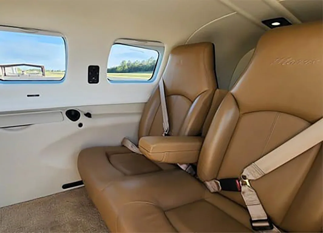 A view of the tan leather passenger seats in the aircraft's cabin, looking towards the rear with windows showing an airfield.