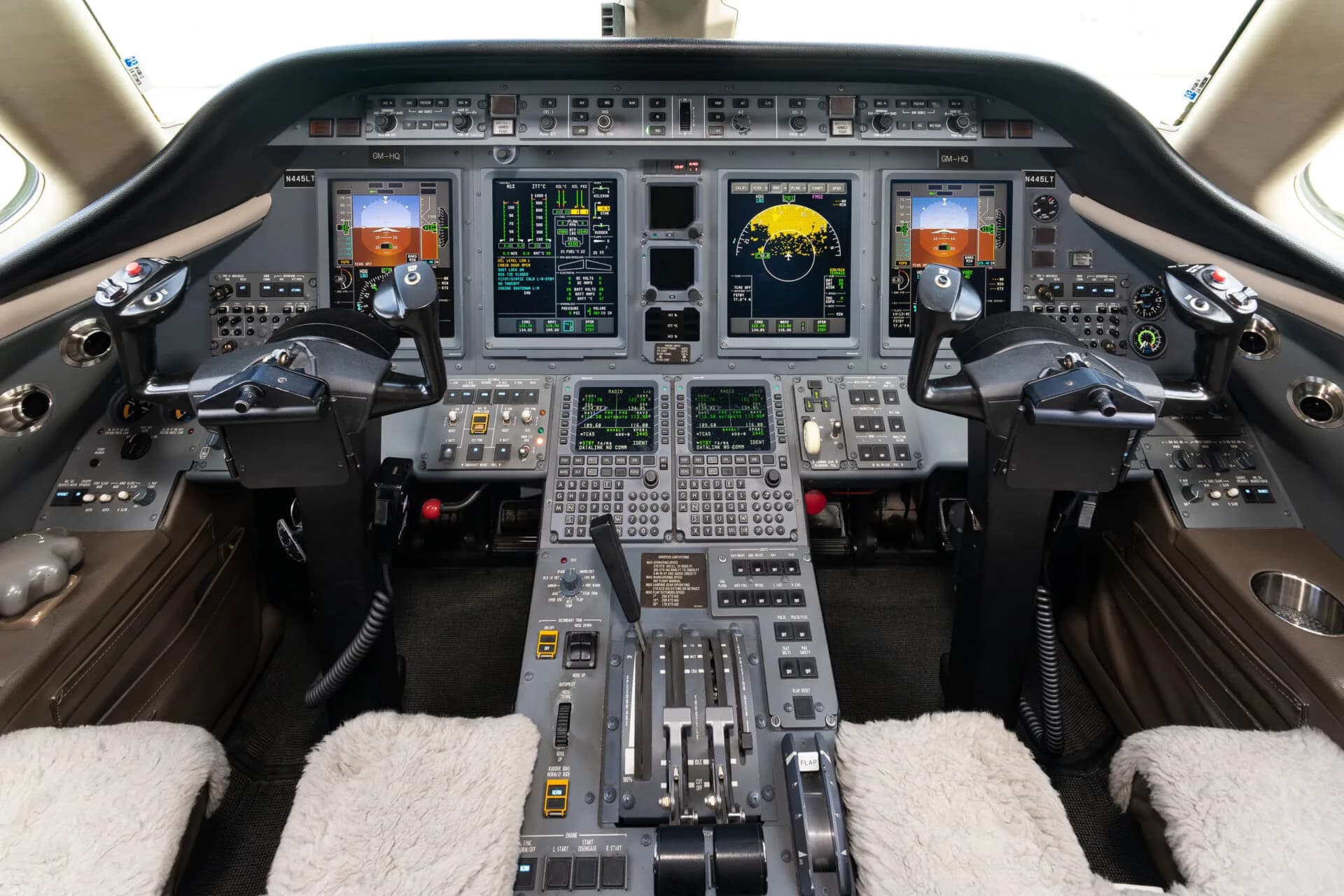 The modern glass cockpit of a business jet with multiple display screens and control yokes.