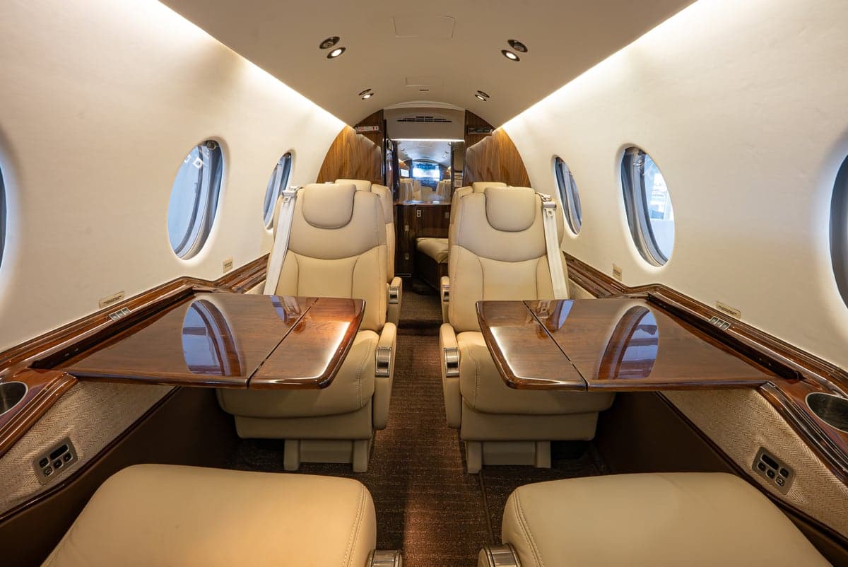View of the Learjet cabin with tan leather seats and wood tables.