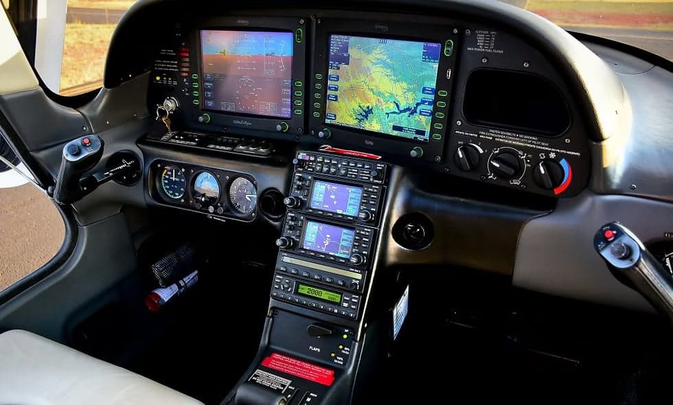 A Cirrus SR22 aircraft is parked on the tarmac with a white and silver paint scheme.