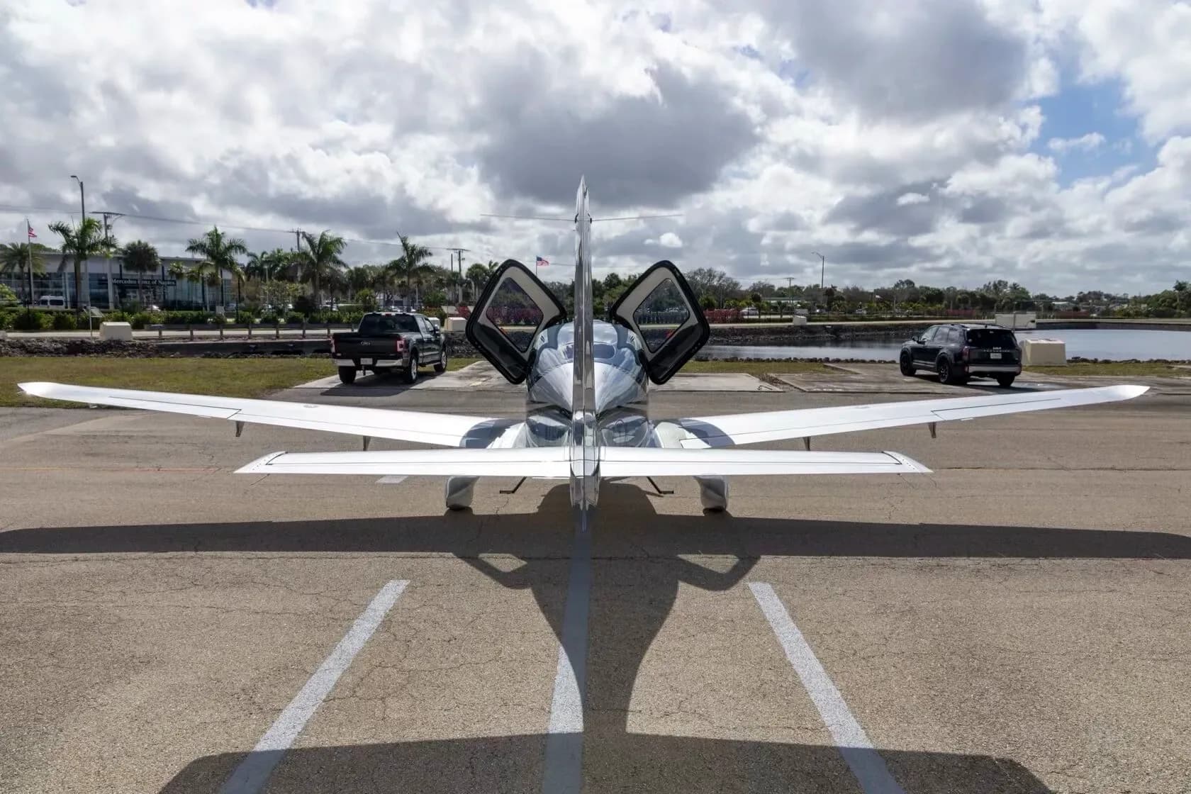 A rear view of a blue and silver Cirrus SR22T aircraft with its gull-wing doors open, parked on an airfield.