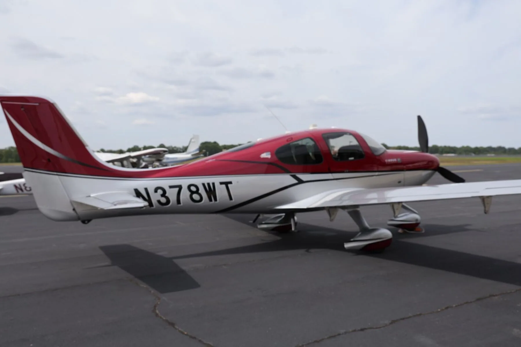 A side view of the red and silver Cirrus SR22T aircraft, N378WT, parked on an airfield.