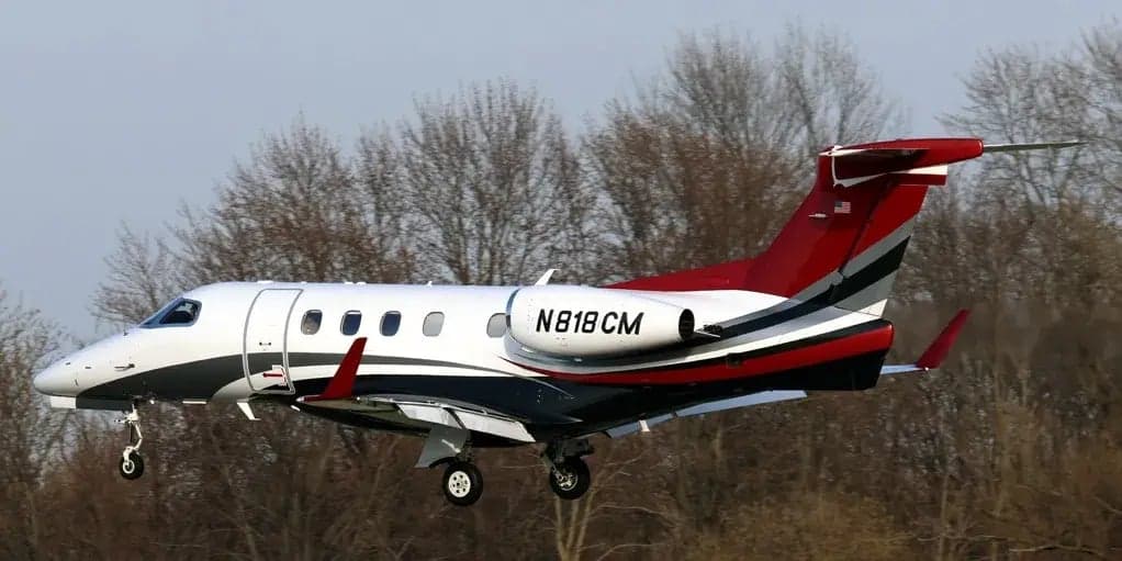Side view of a white and red Phenom 300 aircraft in flight.