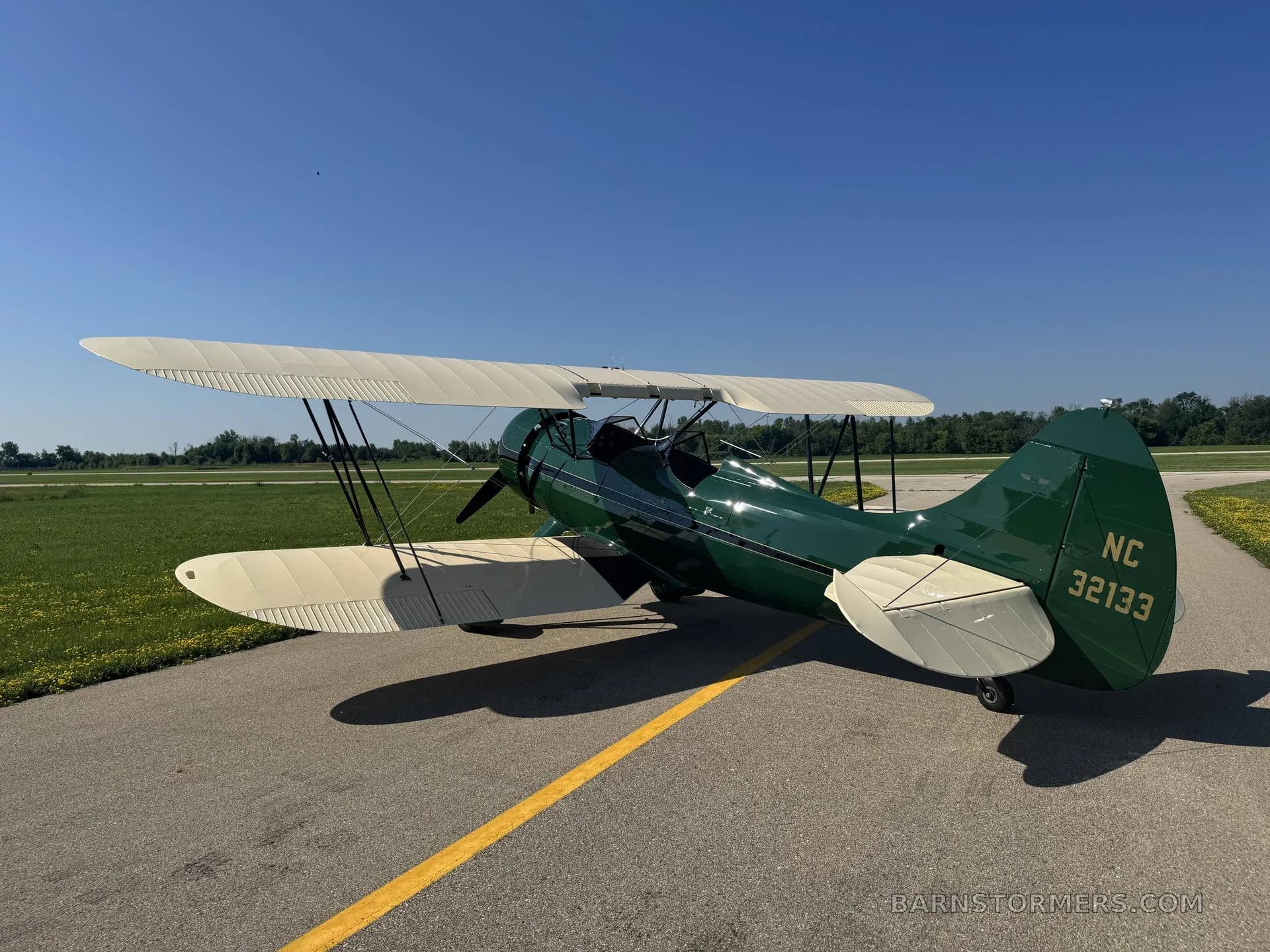 The rear view of a green and cream biplane with registration NC 32133 on its tail, parked on an asphalt runway.