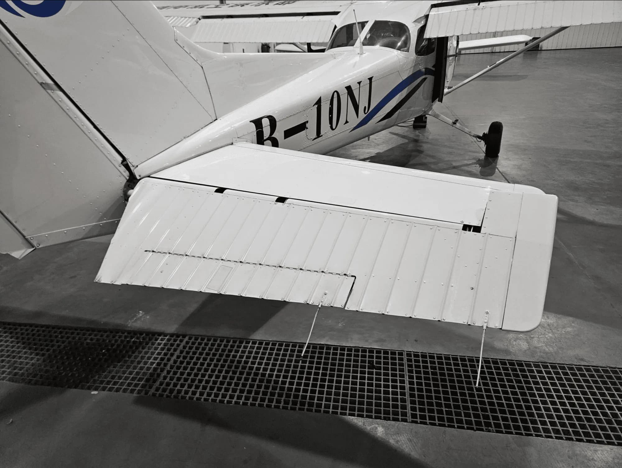 A black and white close-up of the tail and right wing of a white aircraft with registration B-10NJ in a hangar.