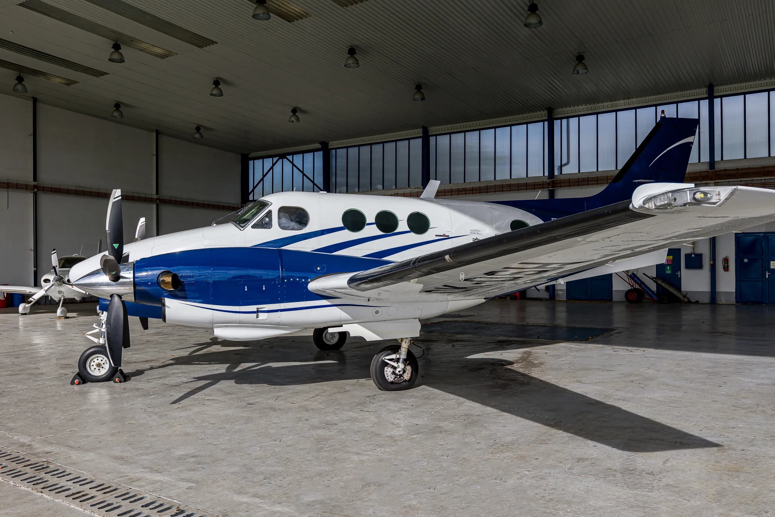 A white and blue twin-engine turboprop aircraft, likely a King Air, parked inside a hangar.