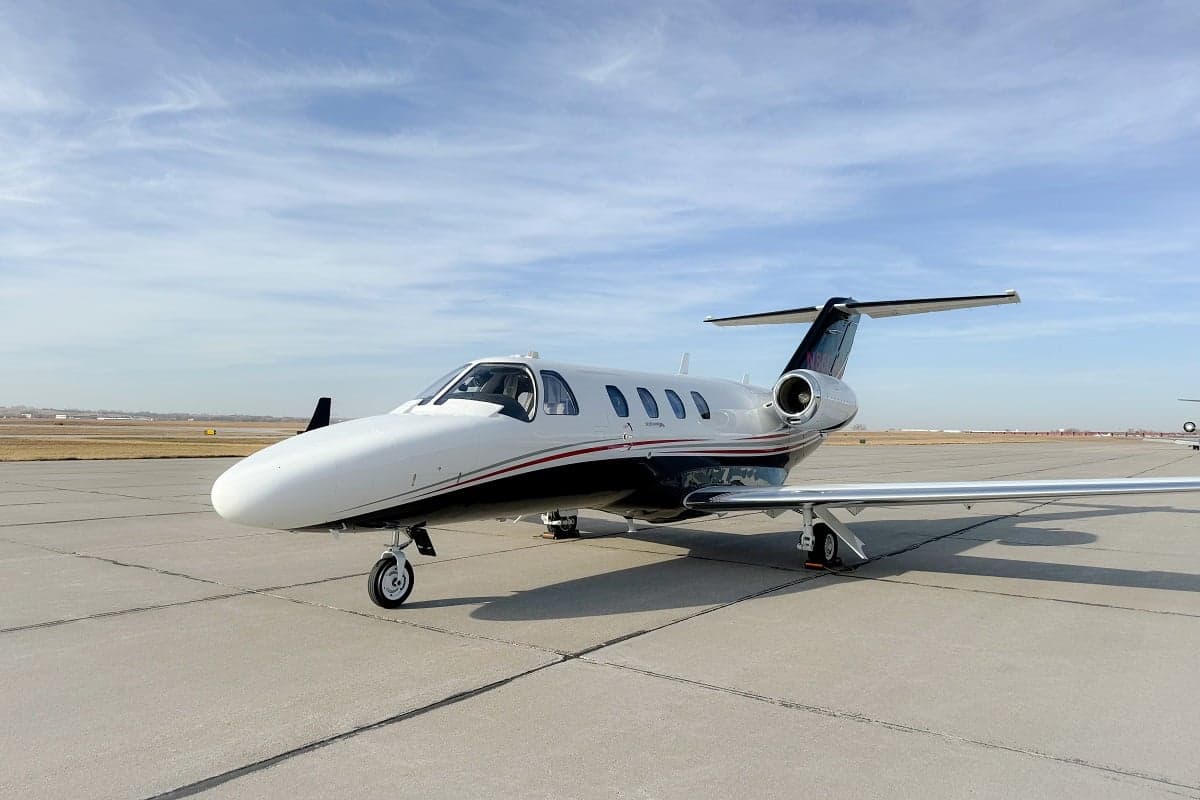 A Cessna Citation CJ3+ aircraft with a white and black paint scheme is parked on the tarmac.