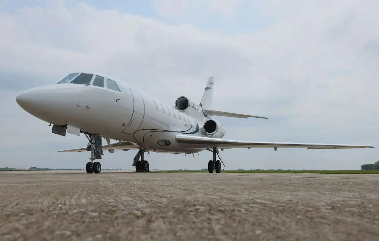 A low-angle view of a white Dassault Falcon business jet with registration N37WX on the tail, parked on an airfield.