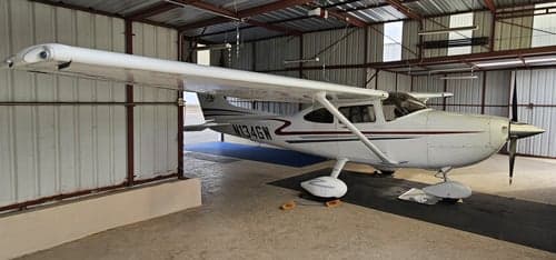 A white Cessna 182 Skylane with red and green stripes, registration N134GW, parked inside a metal hangar.