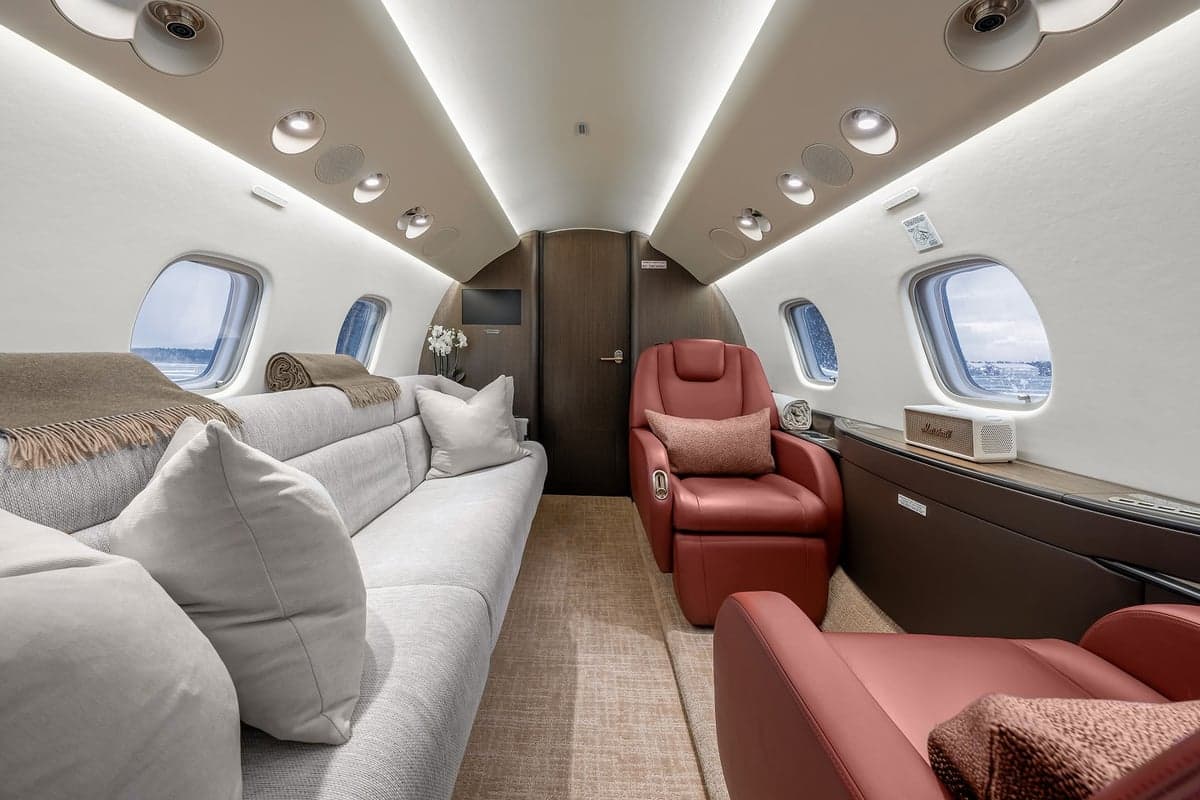 View of the aircraft interior with red leather seats, a couch, and a neutral color scheme.