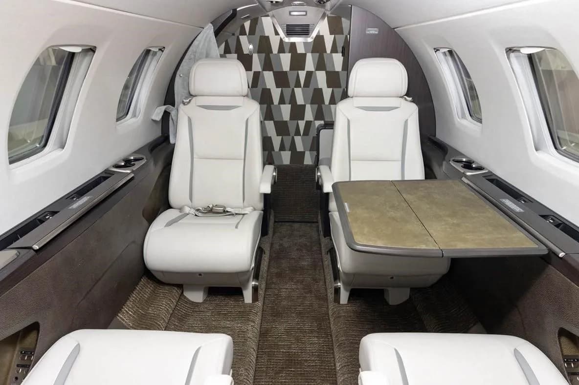 The interior cabin of the Citation M2, showing two white leather passenger seats with a fold-out table between them.