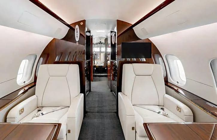 The luxurious interior cabin of a business jet with cream leather seats and dark wood accents.