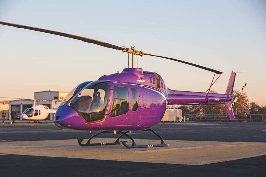 A purple helicopter parked on a tarmac with another helicopter in the background.
