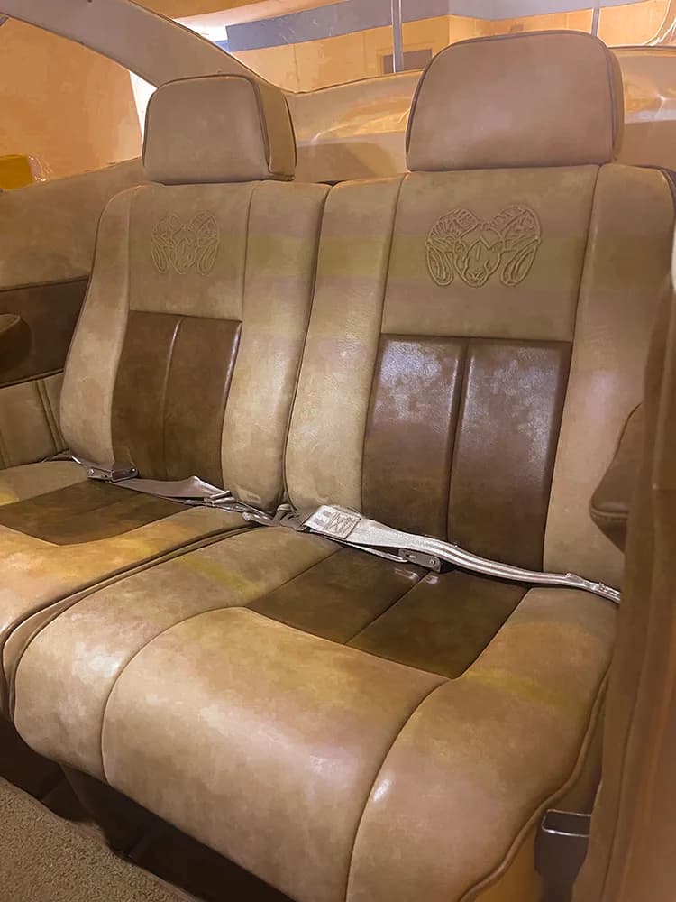A close-up of the tan leather rear seats of an aircraft, with ram's head logos embossed on the headrests.