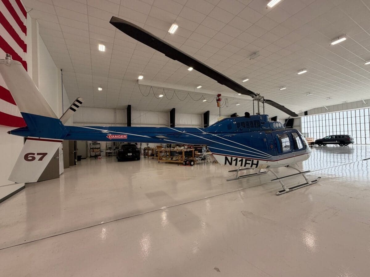 A blue and white Bell 206B JetRanger helicopter parked in a hangar, showing the tail number N11FH.