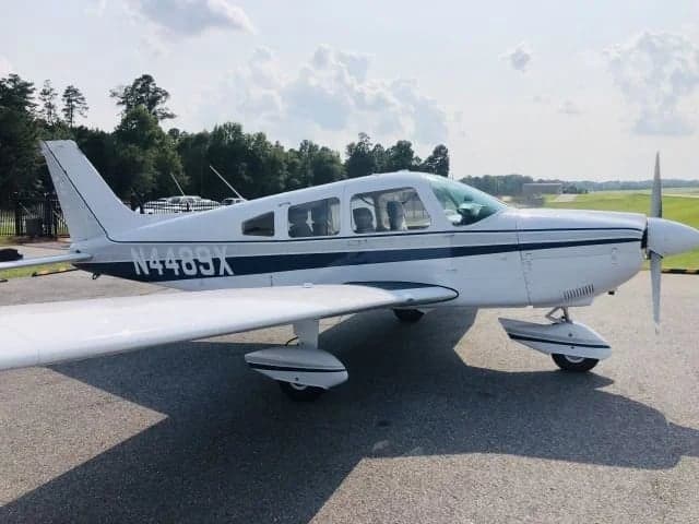 A white and blue single-engine aircraft with tail number N446SX parked on the tarmac.