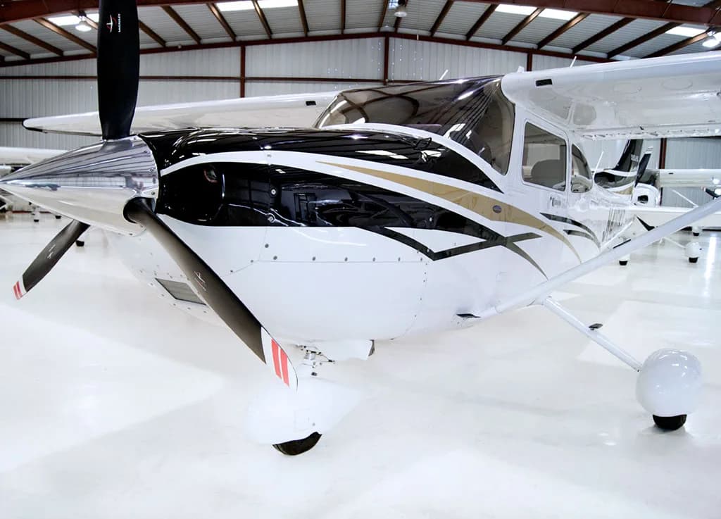 A close-up view of the front propeller and nose of a white Cessna Skylane aircraft with black and gold stripes.