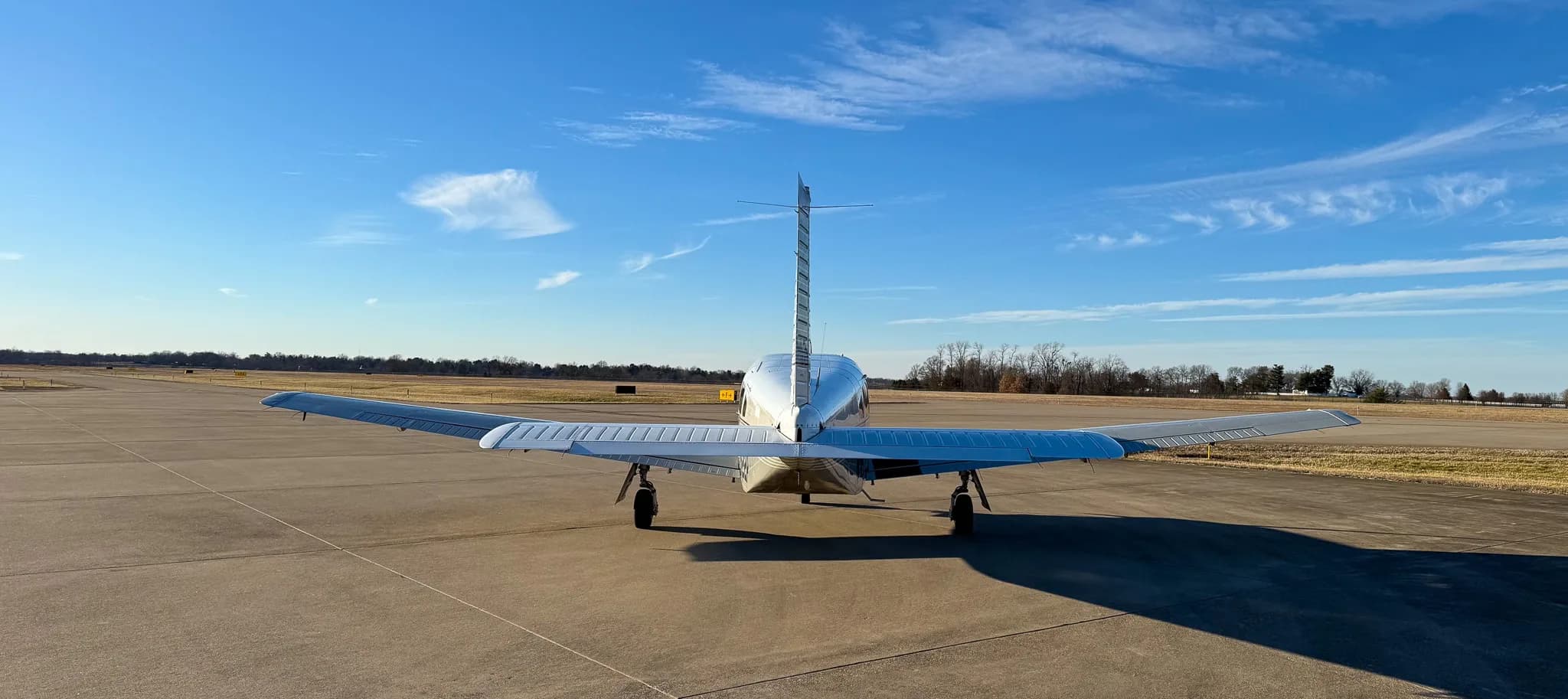 A rear view of a white Piper Saratoga SP (N1622P) with grey stripes parked on an airfield.