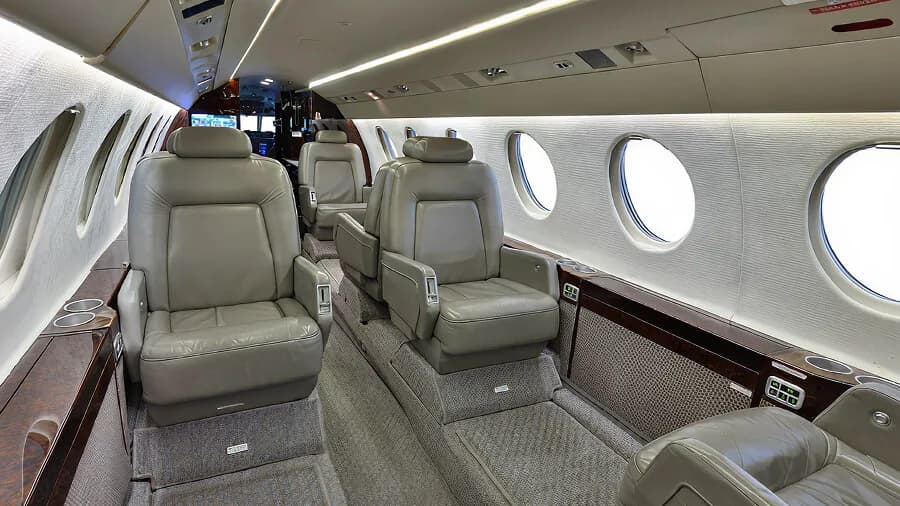 A view of the business jet's cabin with grey leather seats and large oval windows.