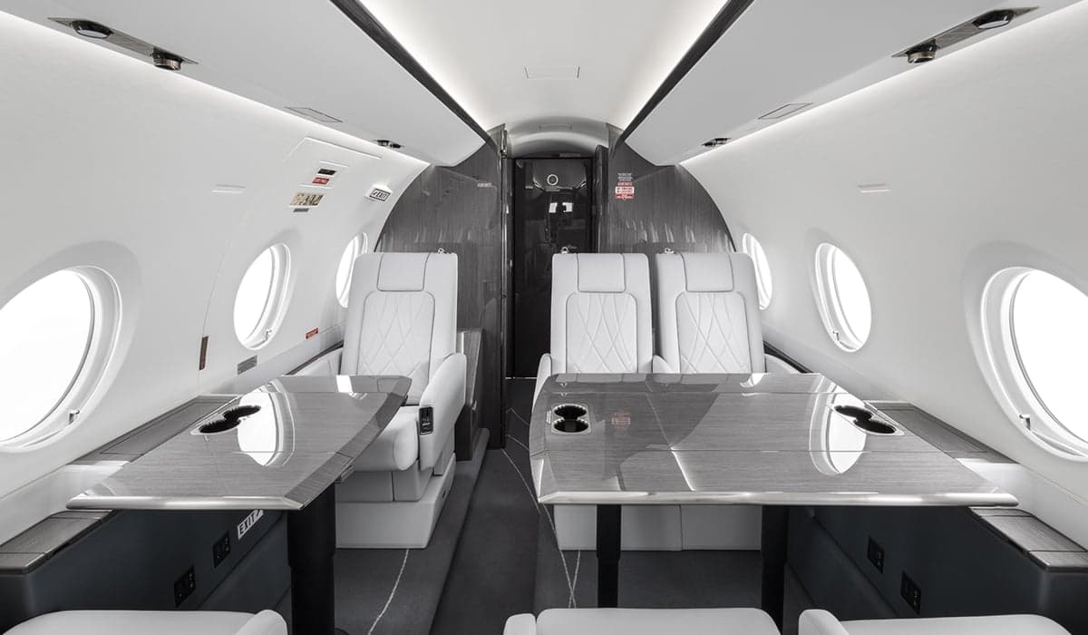 The interior of the aircraft features white leather seats and dark wood tables.