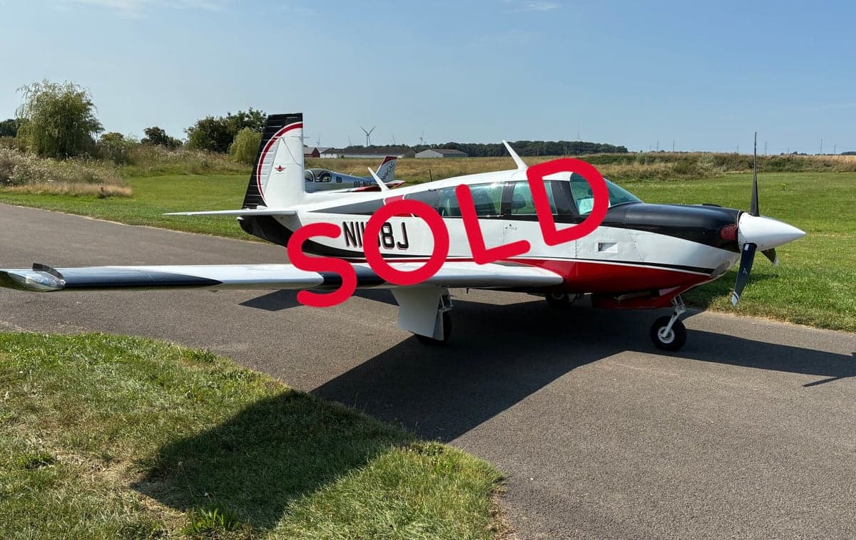 A Mooney M20 aircraft with a black, white, and red paint scheme is parked on the tarmac with the word SOLD overlaid.